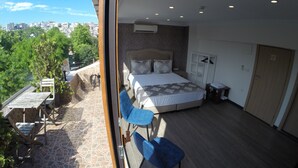 A bedroom with a large bed, a wooden floor, a balcony with a table and chairs, and a city view. - Meydan Suites (Istanbul)
