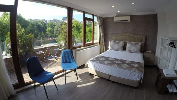 A bedroom with a large bed, two blue chairs, a view of greenery outside, and a white wardrobe. - Meydan Suites (Istanbul)