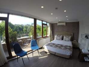 A bedroom with a large bed, two blue chairs, a view of greenery outside, and a white wardrobe.