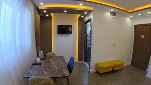 A modern dining area with a marble table, chairs, a television, and a yellow bench. - Meydan Suites (Istanbul)