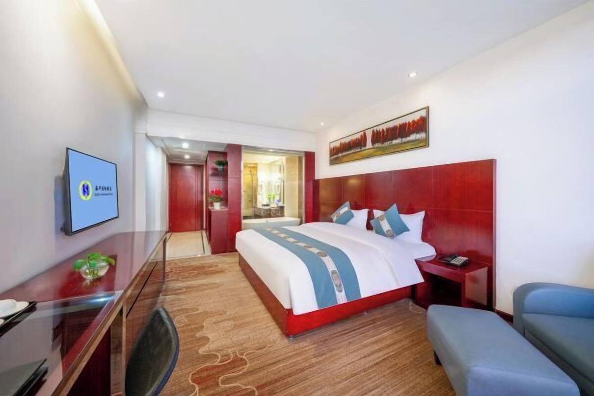 A hotel room with a large bed, a desk, a chair, and a TV.