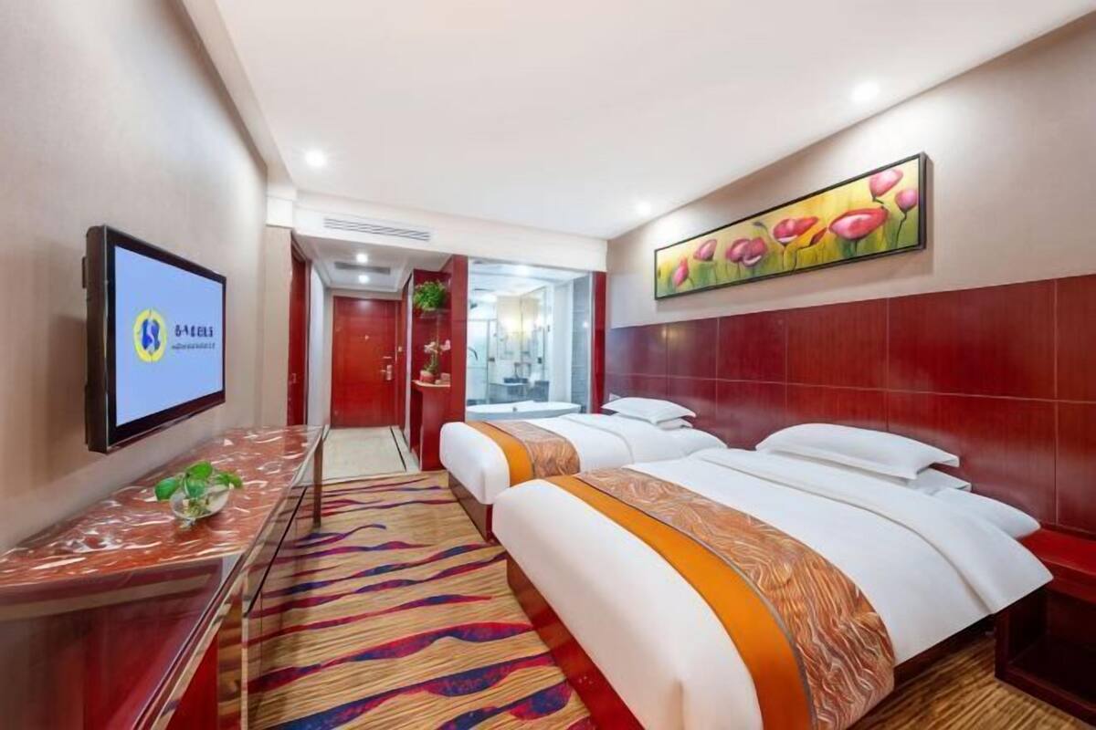 A hotel room with a bed, a TV, a painting, and a carpet.