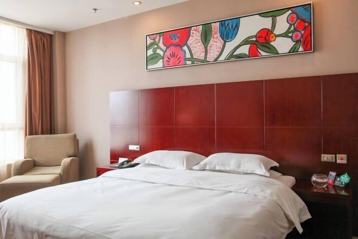A hotel room with a large bed, a chair, a nightstand, and a painting on the wall.
