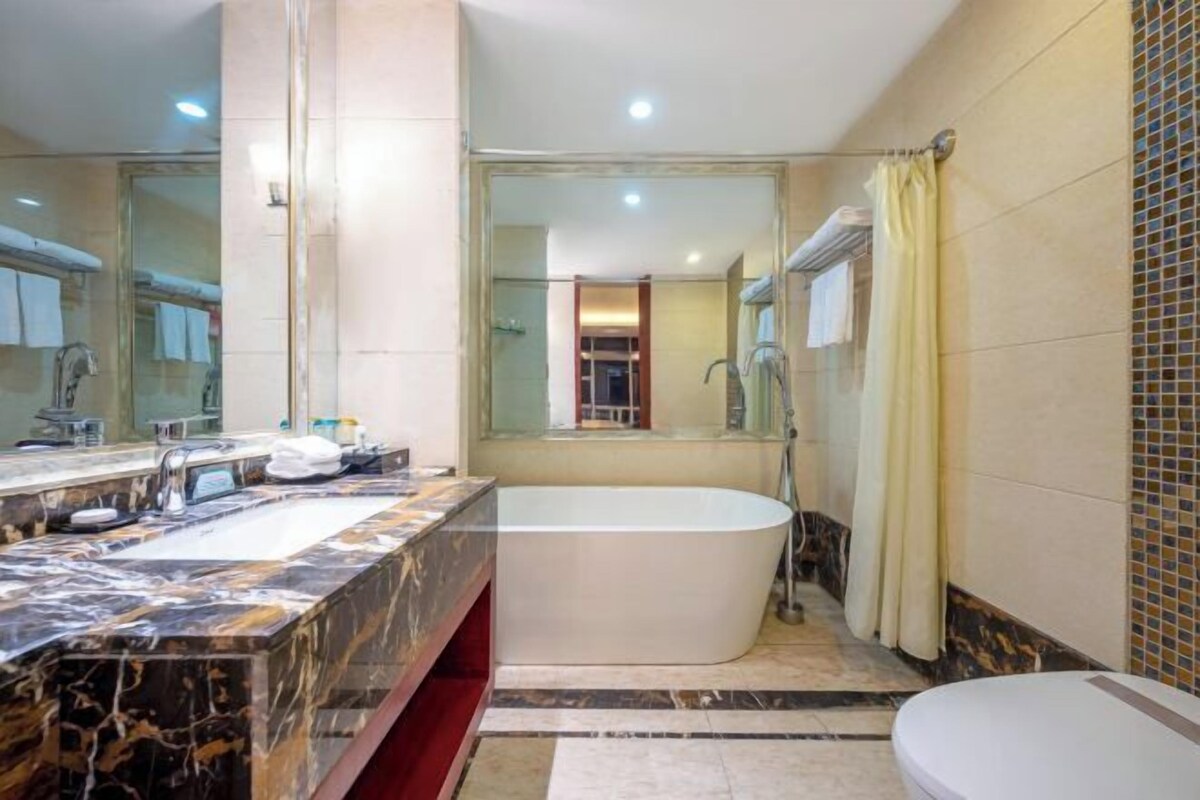Un baño con tocador de mármol, bañera independiente y un espejo grande.