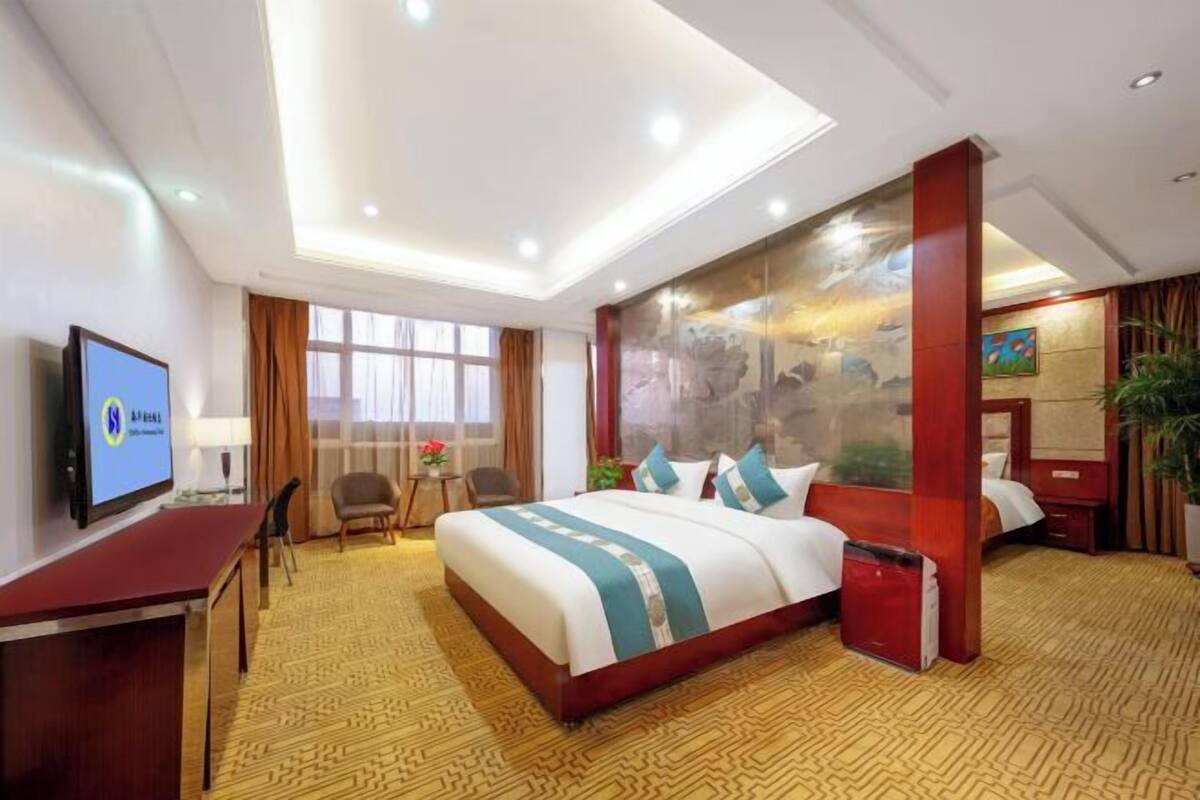 A hotel room with a large bed, a desk, a TV, and a window with curtains.