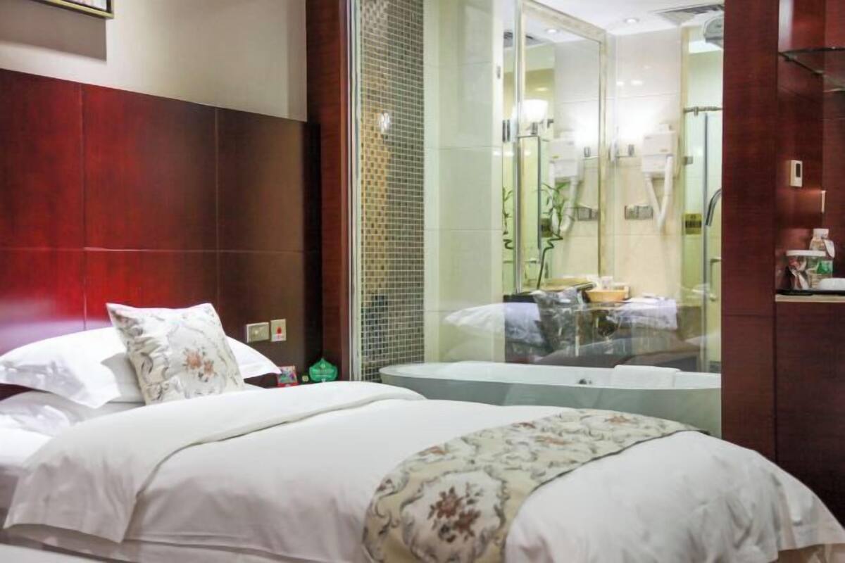 A hotel room with a bed, a glass partition, and a bathroom with a bathtub.