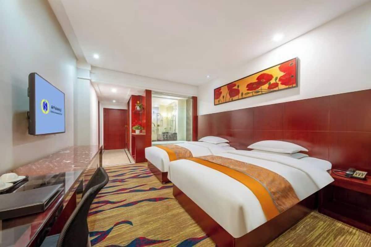 A hotel room with a bed, a desk, a television, and a painting on the wall.