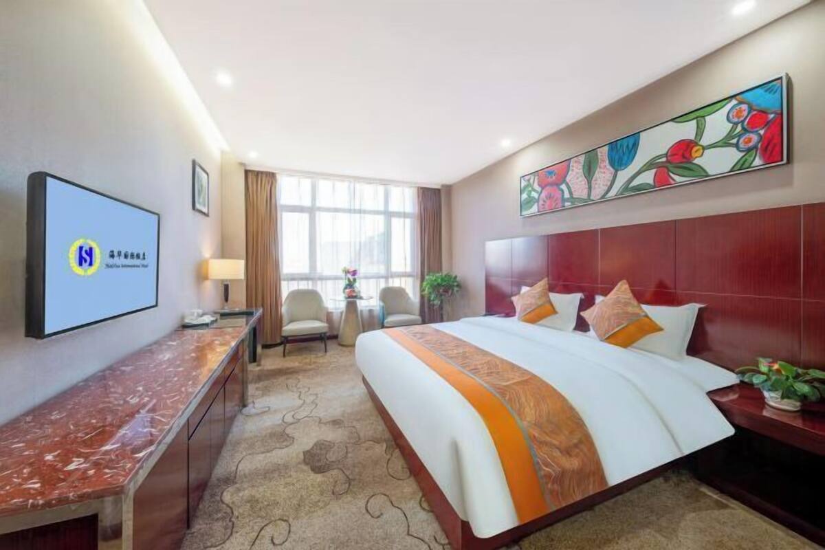 A hotel room with a large bed, a desk, a TV, and a painting on the wall.