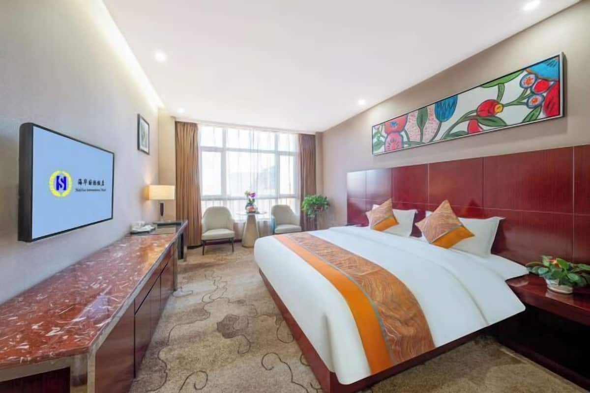 Habitación de hotel con una cama grande, un escritorio, un televisor y un cuadro en la pared.
