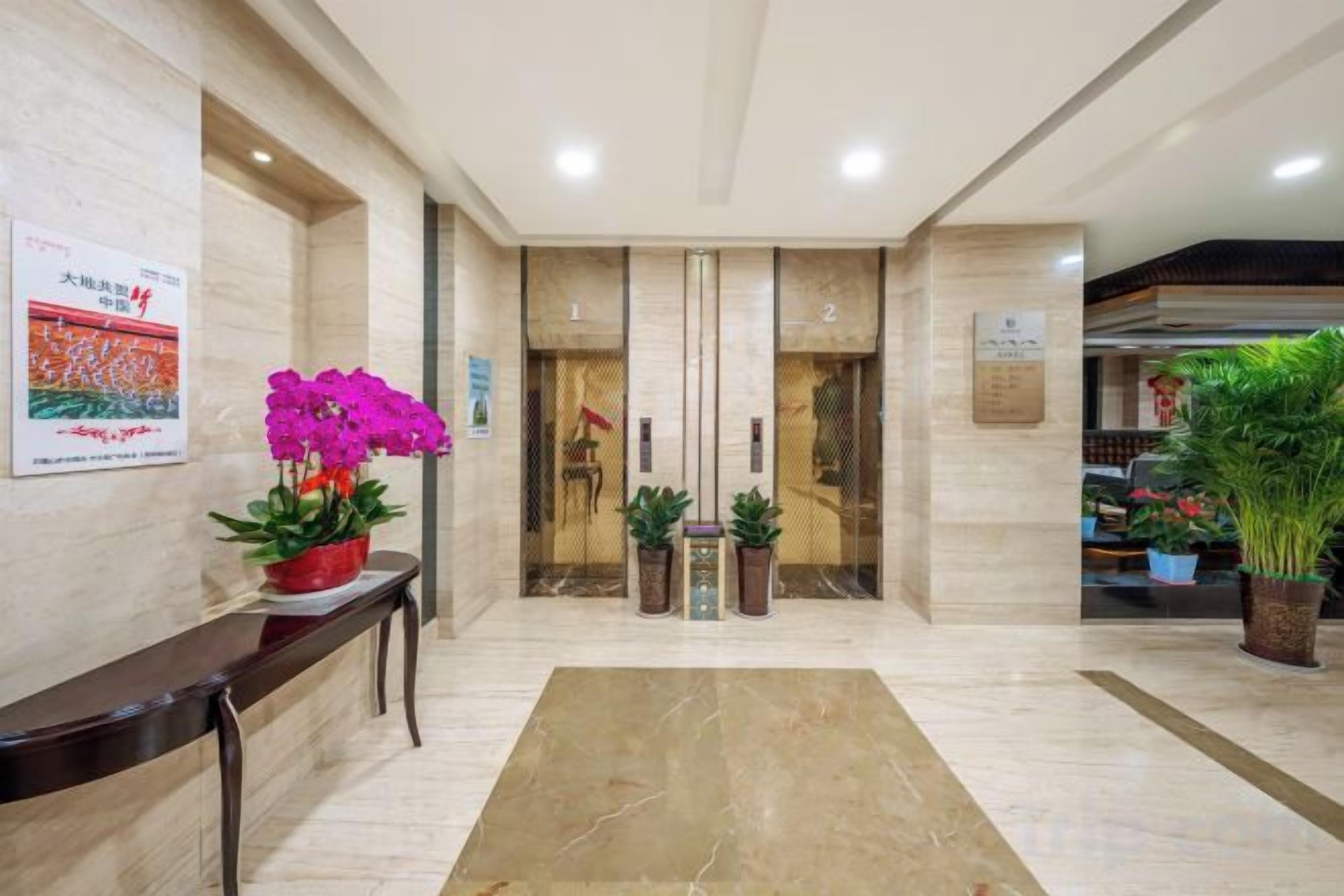 A hotel lobby with a reception desk, potted plants, and a marble floor.