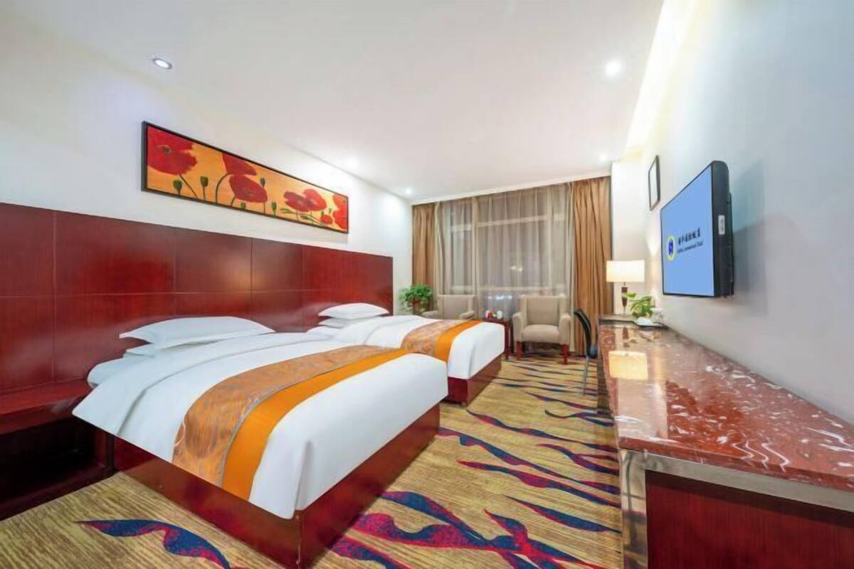 A hotel room with two beds, a TV, a desk, and a large window with curtains.