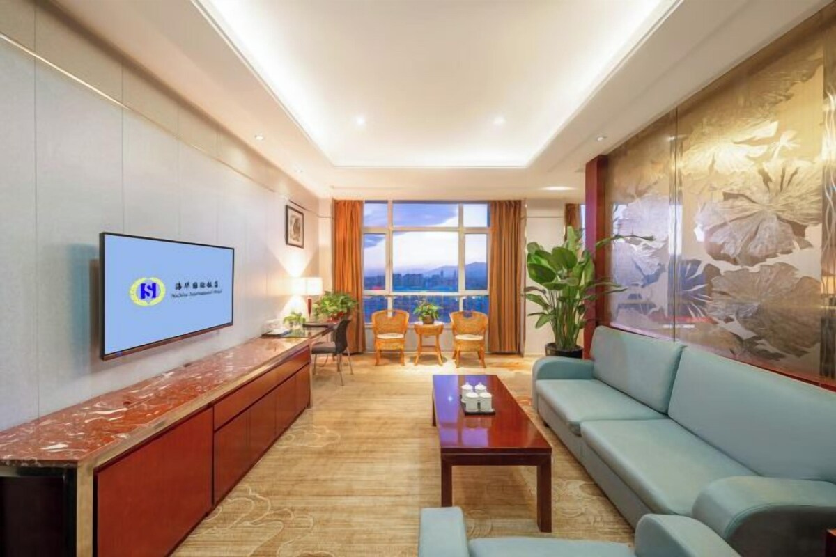 Una sala de estar moderna con un sofá, una mesa de centro, un televisor montado en la pared y vistas de la ciudad a través de amplias ventanas.