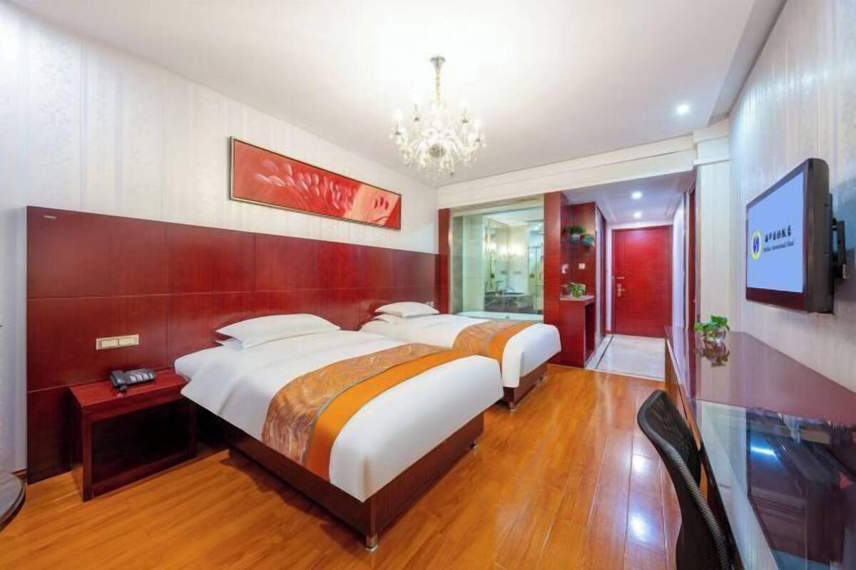 A hotel room with two beds, a TV, a chandelier, and a wooden floor.
