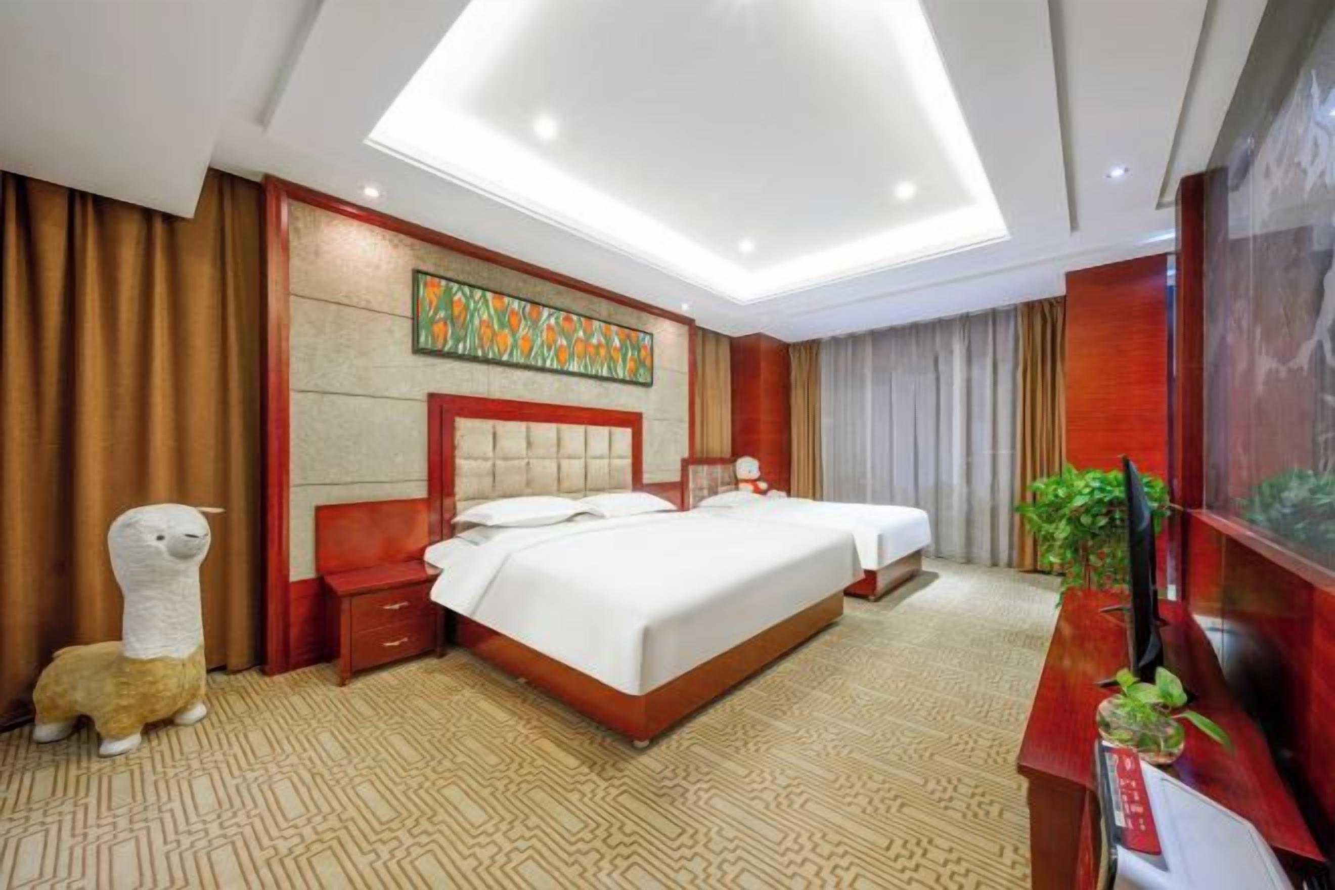 A hotel room with a large bed, a desk with a plant, and a decorative wall piece.