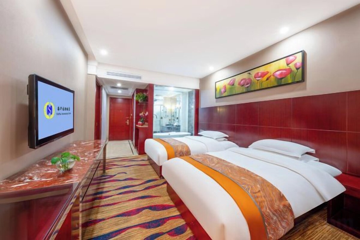 Una habitación de hotel con una cama, un televisor, una pared roja y un cuadro.