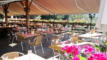 An outdoor dining area with tables and chairs, covered by a canopy, and surrounded by flower arrangements.