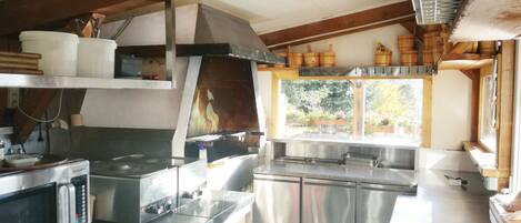 A kitchen with stainless steel appliances, wooden barrels, and a window with a view of greenery.