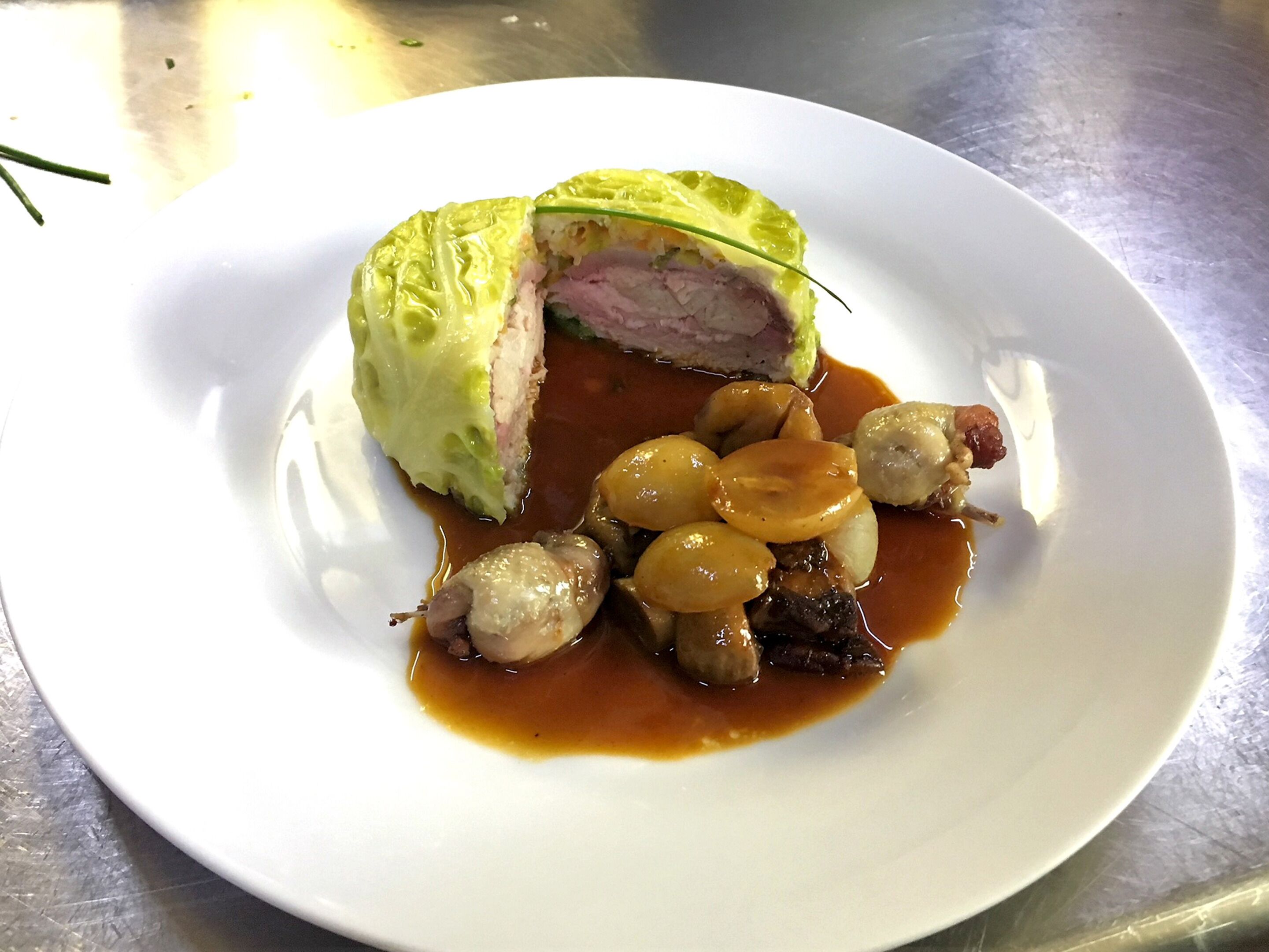 Un plato con un guiso de carne, posiblemente un rollo de carne, acompañado de pequeñas esferas y salsa marrón.