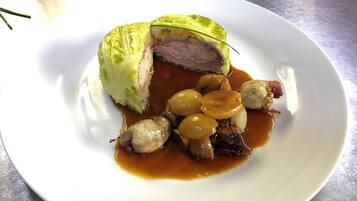 Un plato con un guiso de carne, posiblemente un rollo de carne, acompañado de pequeñas esferas y salsa marrón.