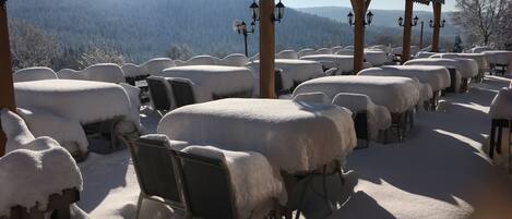 Een overdekt buitengebied met tafels en stoelen bedekt met sneeuw, houten pilaren en hangende lantaarns.