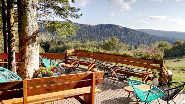 Eine Holzterrasse mit Bänken und Stühlen mit Blick auf ein bewaldetes Tal.