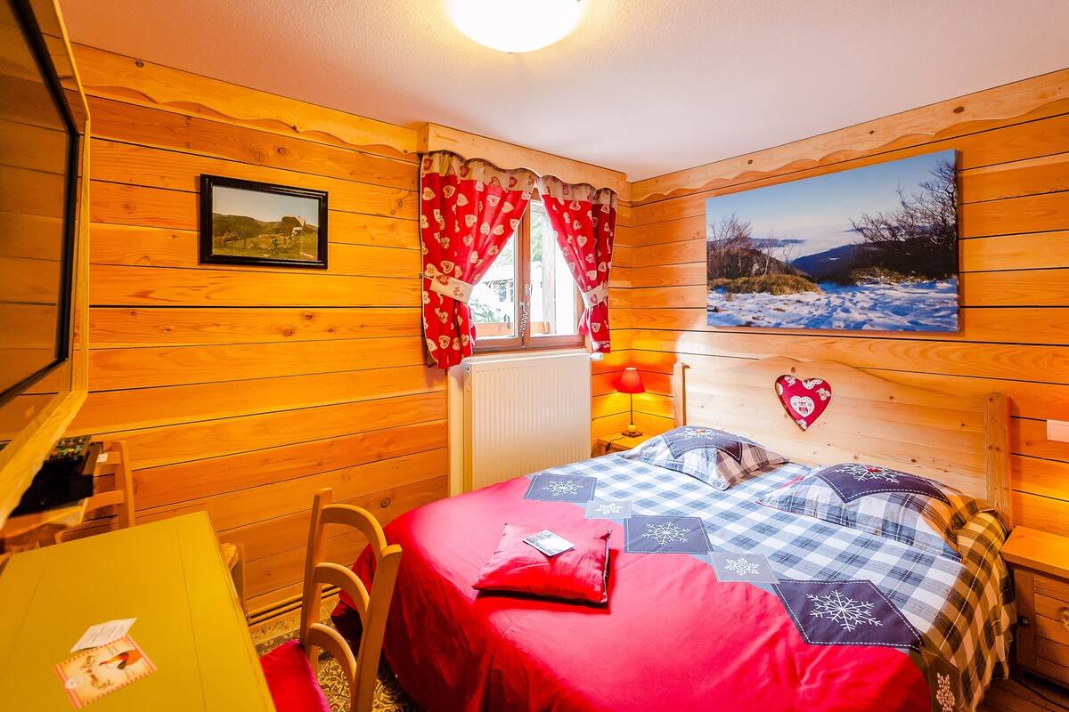 A cozy wooden room with a bed, a desk, and a window with curtains.