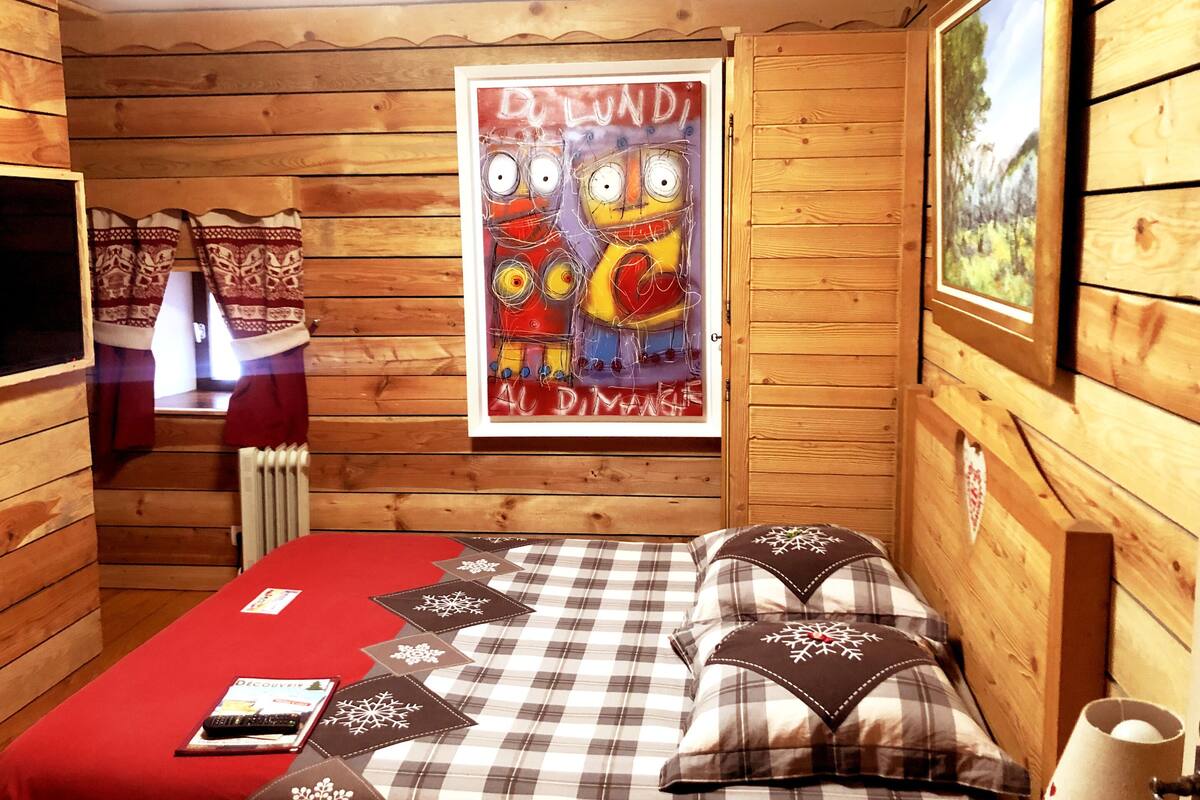 A wooden cabin room with a bed, a poster, and a window.