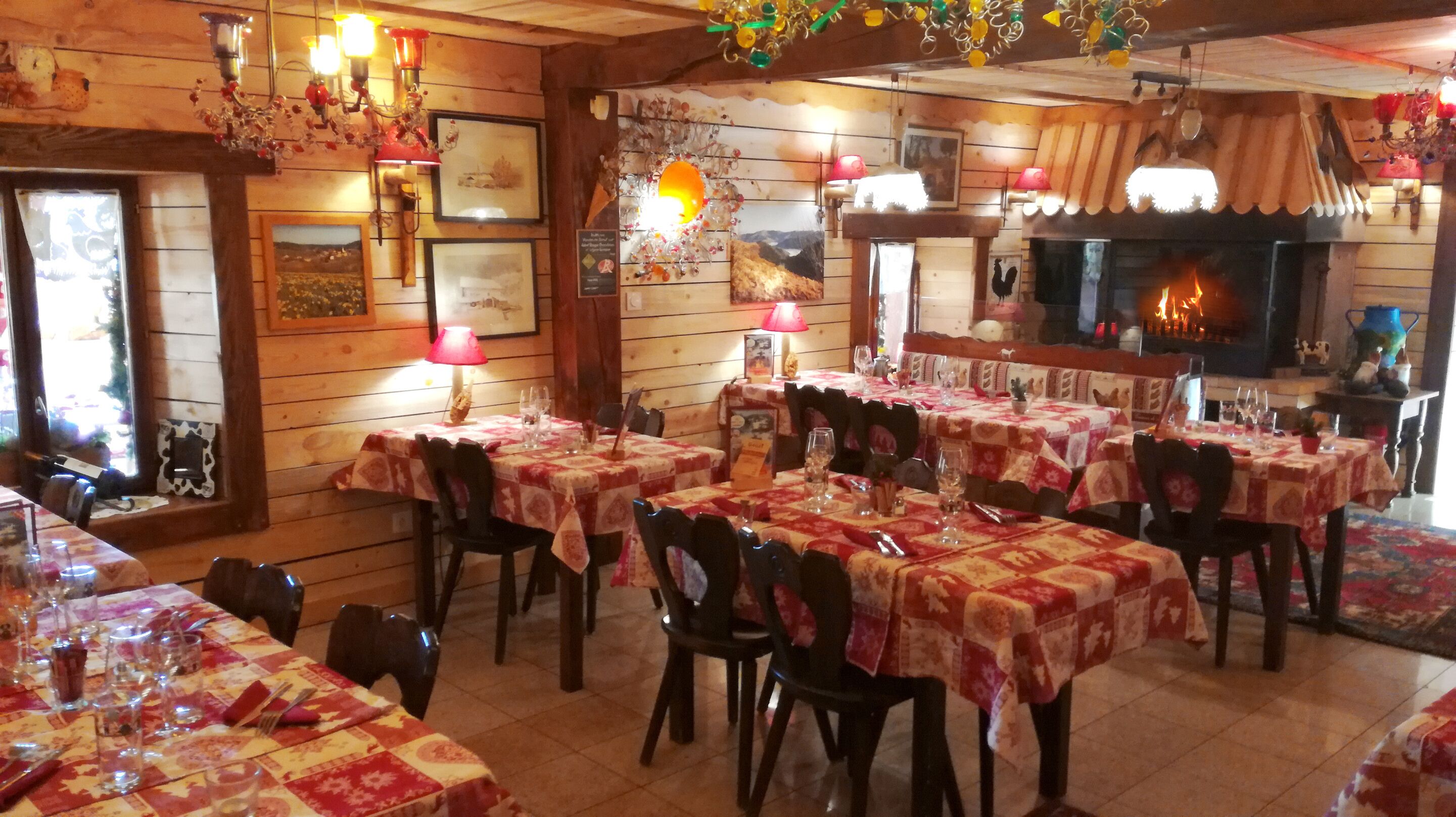 Un restaurante acogedor con paredes de madera, varias mesas con manteles rojos y blancos, y una chimenea.