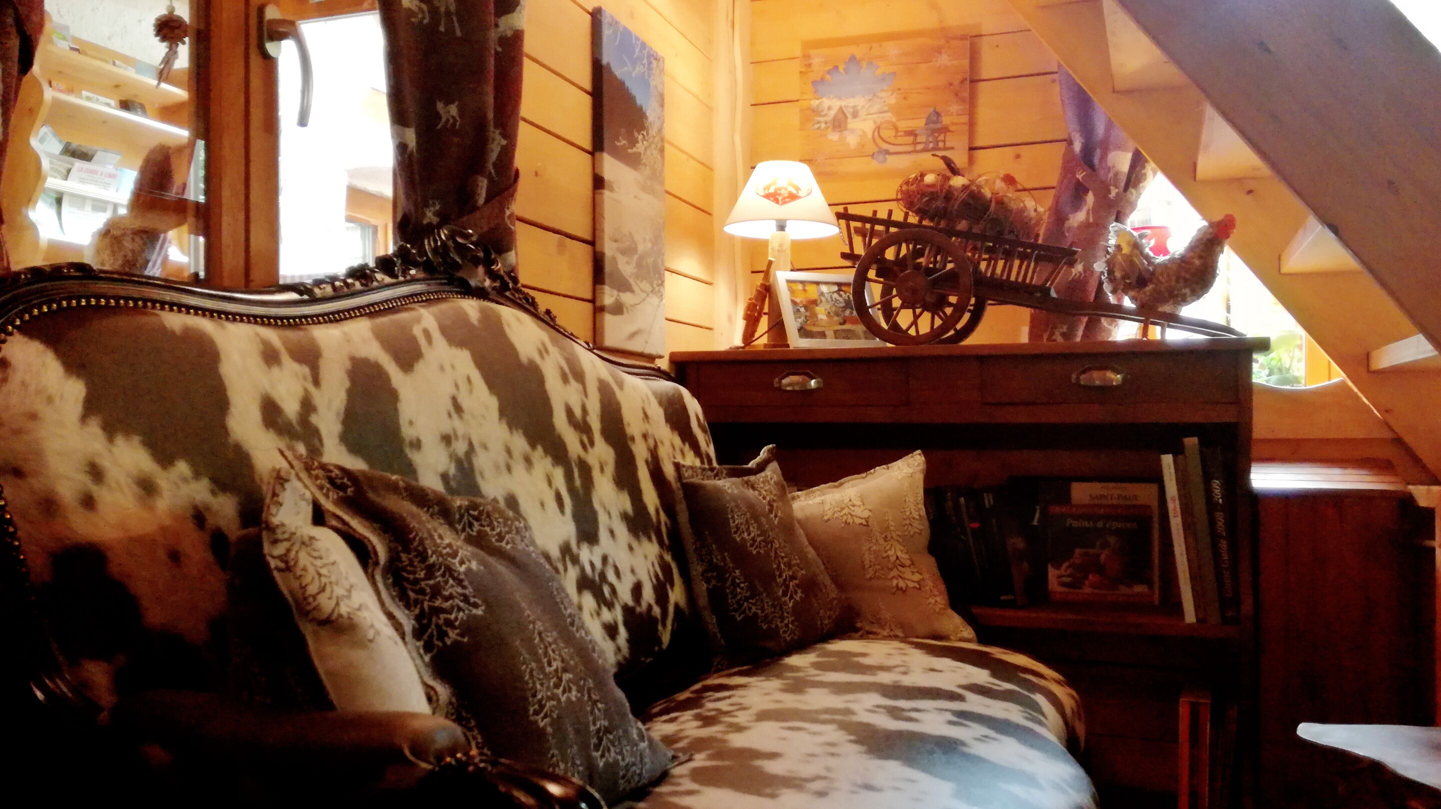 A cozy room with a patterned sofa, a lamp, a wooden side table with a lamp, and a wall with a rustic painting.