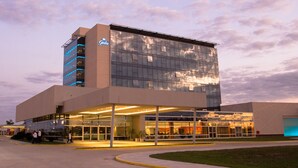A modern hotel with a glass facade, a prominent crown logo, and a well-lit entrance area.
