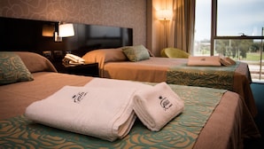 A hotel room with two beds, a nightstand with a lamp, and a view of the outdoors.