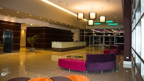 A modern lobby with a reception desk, seating area, and glass doors leading to an outdoor space.