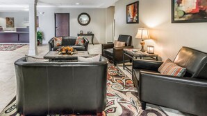 A modern living room with leather sofas, a coffee table with decorative items, a lamp, and a reception desk in the background.