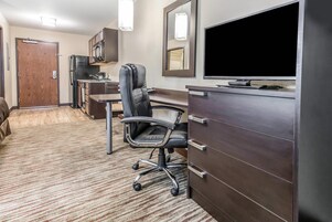 Habitación de hotel con escritorio, silla, televisión, minibar y puerta que da a un baño.
