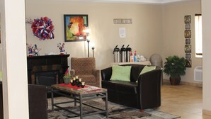 A lobby with a fireplace, seating area, coffee station, and decorative wall art. - Suburban Studios Washington, PA (Washington)