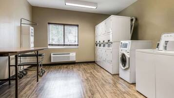 A laundry room with a large window, a cart, and stacked cabinets.