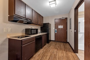 A compact kitchen with dark wooden cabinets, a microwave, a refrigerator, and a wooden floor. - Suburban Studios Washington, PA (Washington)