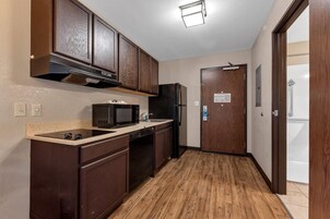 Una cocina compacta con armarios de madera oscura, microondas, refrigerador y piso de madera.
