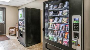 A vending machine and a refrigerator in a room with tiled flooring and a door with a window view.