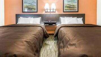 A hotel room with two beds, a nightstand, two wall-mounted lamps, and two framed artworks above the beds.