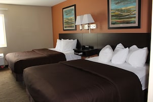 Quarto de hotel com duas camas, uma mesa de cabeceira e duas pinturas na parede.