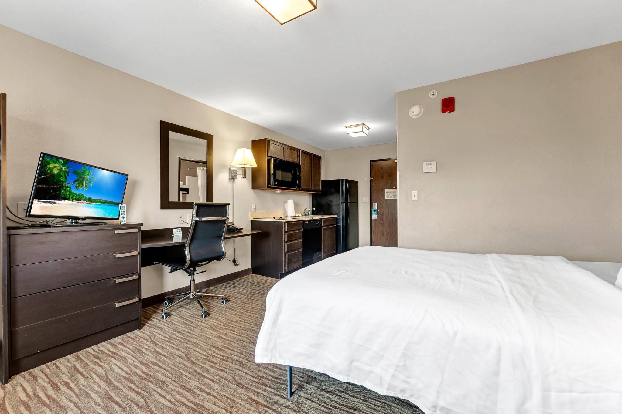 Une chambre d’hôtel comprenant un lit, un bureau, une chaise, une télévision, une kitchenette et une porte de salle de bain.