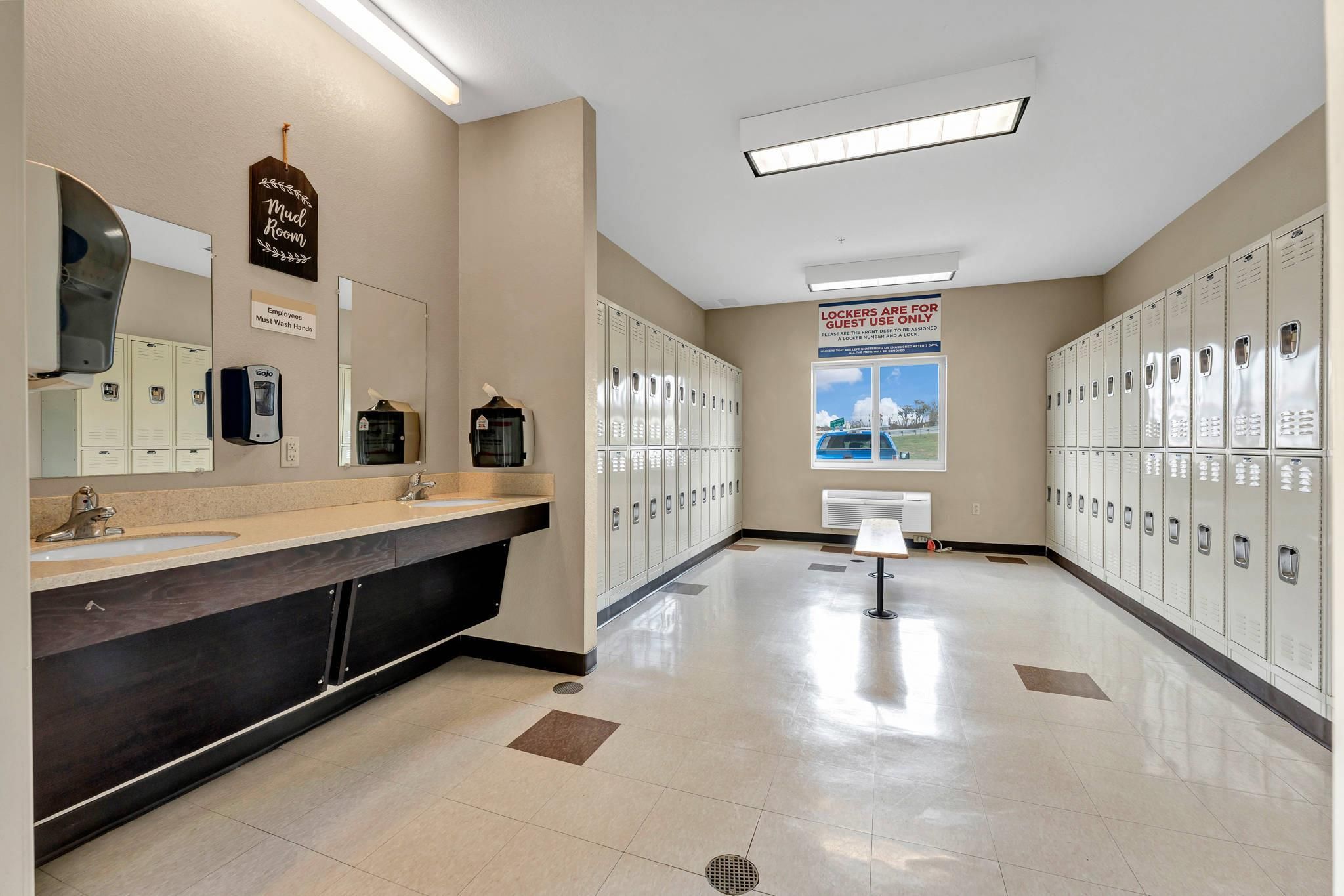A clean, well-lit locker room with multiple lockers, a sink, and a mirror.