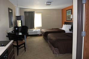 A hotel room with a desk, two beds, a window with curtains, a painting on the wall, and an air conditioning unit. - Suburban Studios Washington, PA (Washington)