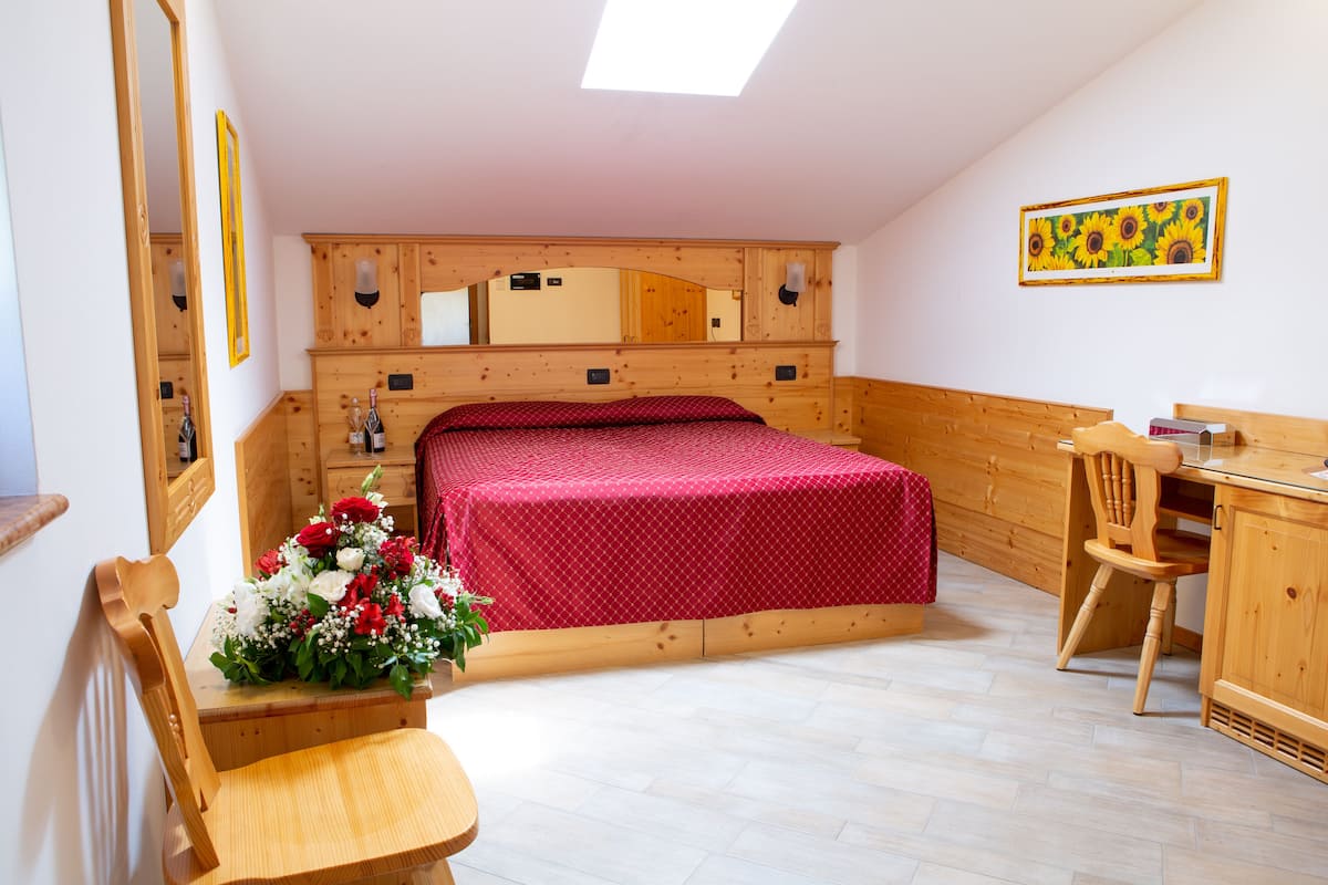A bedroom with a wooden headboard, a bed with a red bedspread, a wooden desk, a chair, and a mirror.