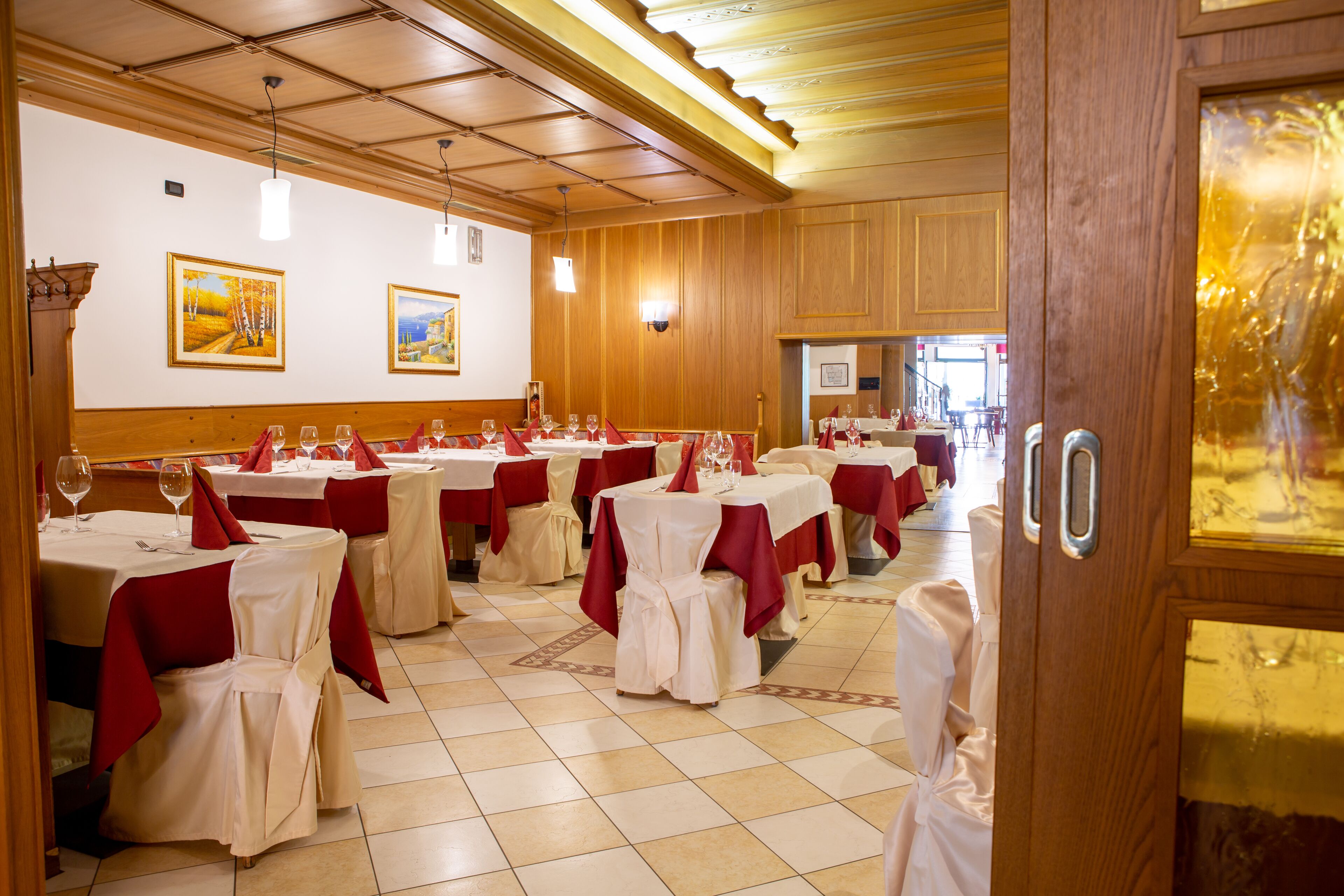 Un salón de banquetes con mesas redondas cubiertas con manteles blancos y caminos de mesa rojos, con sillas adornadas en blanco y rojo.