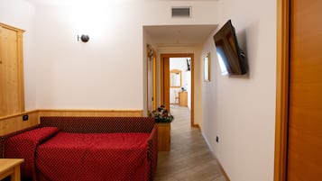 Une chambre d’hôtel avec une armoire en bois, un lit recouvert d’une courtepointe rouge, un téléviseur fixé au mur et un couloir menant à la salle de bain.