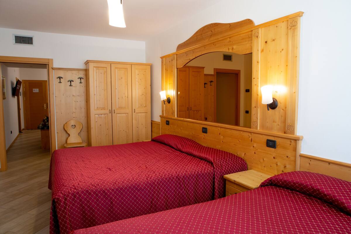 A room with two beds, wooden wardrobe, and a large mirror.