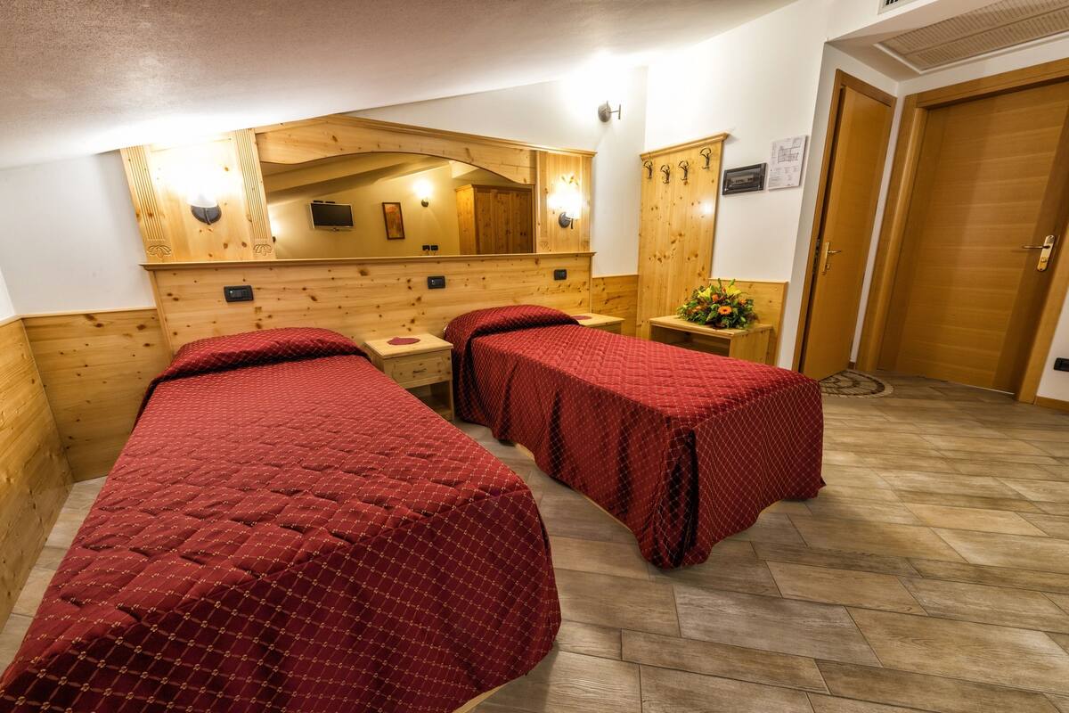 A room with two beds, wooden walls, a mirror, and a wooden wardrobe.