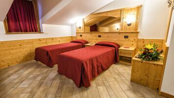 Une chambre avec deux lits, des murs en bois, un plancher en bois, une fenêtre avec des rideaux rouges, un miroir et une petite table sur laquelle est posée une plante.
